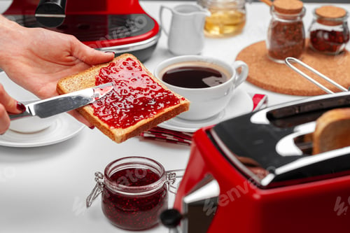 Preview: Female hand spresding strawberry jam on baked toast