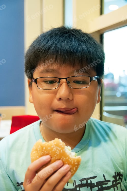 Preview: Portrait of hungry tween boy holding a burger and licking lips.