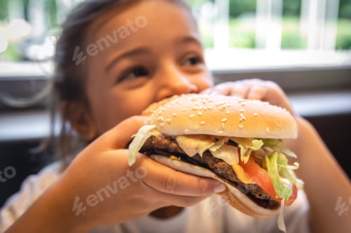 Preview: A little girl eats an appetizing burger, close-up.