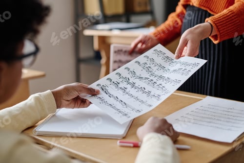 Visualização: Professor irreconhecível dando partituras para criança