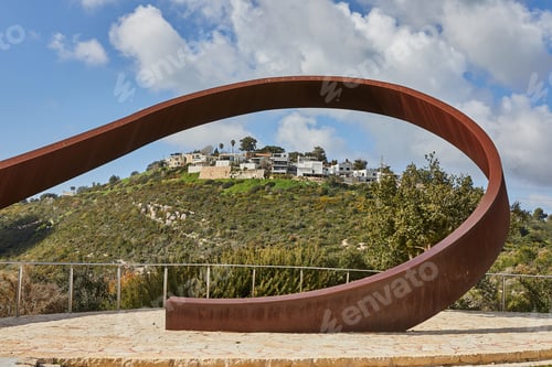 Preview: Rocky hill with a dirt road in front under a blue sky with white clouds and a modern villa on top