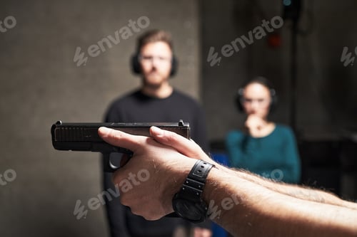 Preview: Man Holding Handgun at Shooting Range with Young Adults Observing