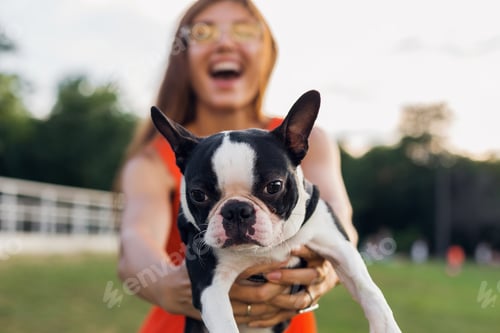 Preview: young happy smiling woman in orange dress having fun playing with dog in park