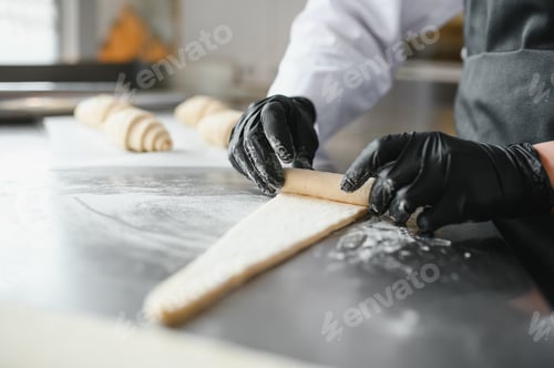 Preview: Baker rolling dough for croissants in bakery kitchen