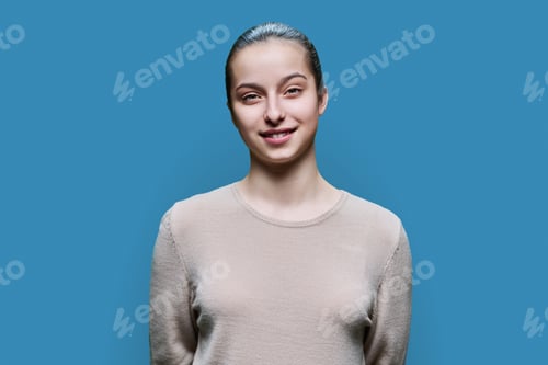 Preview: Portrait of teenage girl 15, 16 years old, smiling looking at camera on blue background