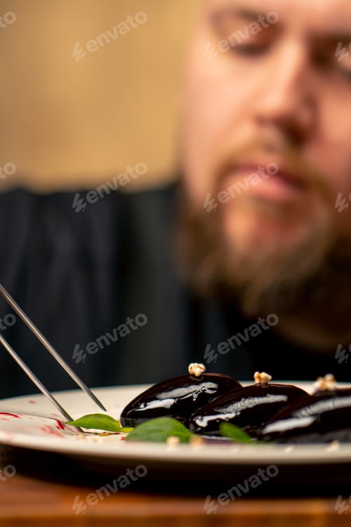 Preview: close-up in a professional kitchen, the chef in black gloves decorates the dessert with tweezers