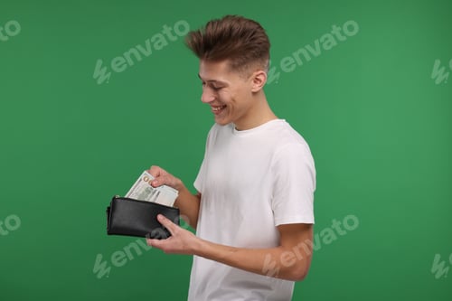 Preview: Happy man putting money into his wallet on green background