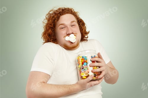 Preview: Portrait of cheerful young European overweight obese male with curly ginger hair consuming junk good