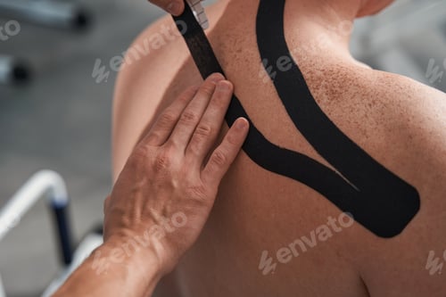 Preview: Physiotherapist treats patient shoulder pain with kinesio tape close up