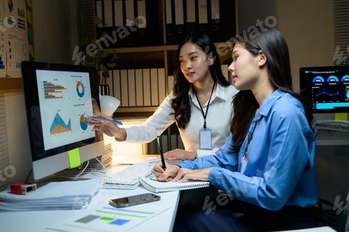 Preview: Two businesswomen working late at night discussing graphs on a computer screen