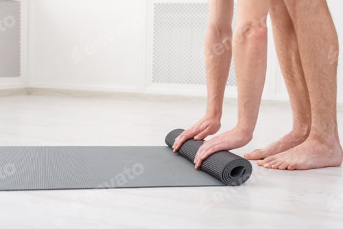 Preview: Man Rolling Out Yoga Mat for Exercise Indoors