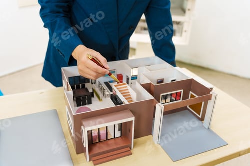 Preview: Asian architect in a suit works alone with laptop, paperwork, blueprints for mortgage project.