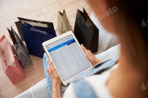 Preview: Woman With Shopping Bags Checks Bank Statement On Digital Tablet