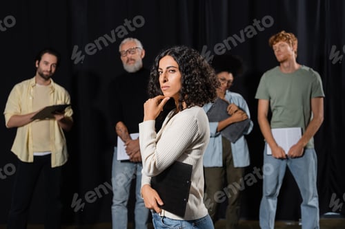Preview: multiracial woman with strict face expression looking at camera while rehearsing near art director