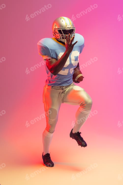Preview: African american male american football player holding ball with neon pink lighting