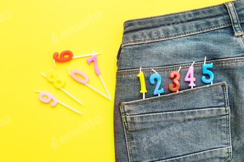 Visualização: velas de aniversário saindo do bolso traseiro de jeans azul em fundo amarelo Número 0-9