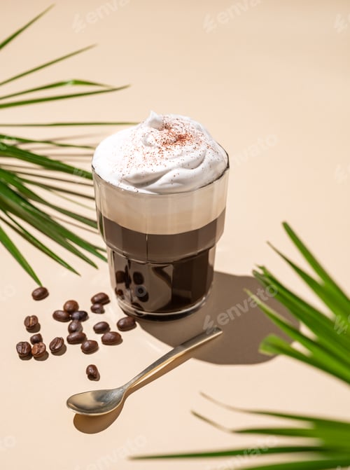 Preview: Iced coffee in a glass with foam on a yellow background with coffee beans, palm leaf and shadows.