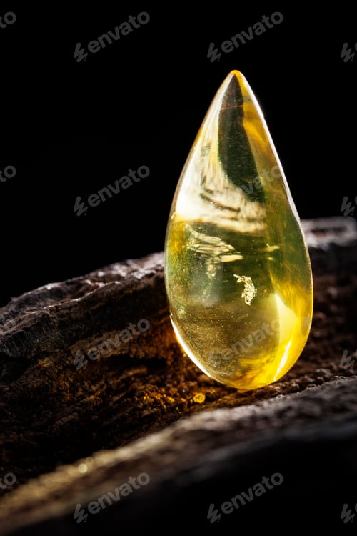 Preview: Natural amber. A piece of yellow transparent natural amber on large piece of dark stoned wood