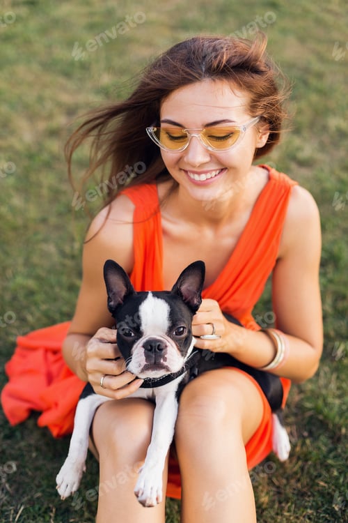 Preview: young happy smiling woman in orange dress having fun playing with dog in park