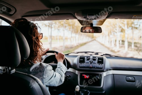 Preview: young beautiful woman driving a van by a path of trees. travel concept, view from inside