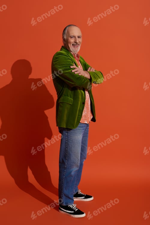 Preview: full length of handsome and bearded senior man standing with folded arms and smiling at camera