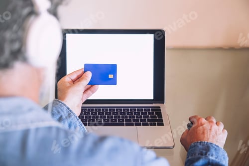 Preview: Closeup of man in front of a laptop with a blue credit card in his hand doing an online shopping