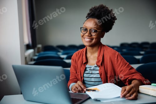 Preview: Happy black female student using laptop while learning in the classroom and looking at camera.