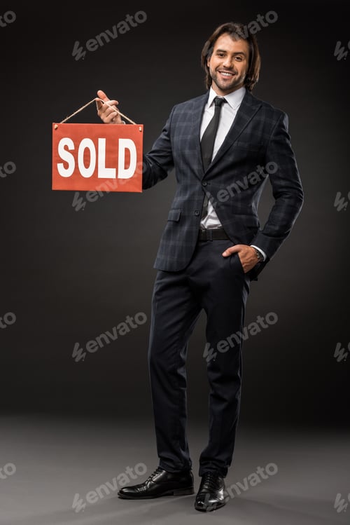 Preview: handsome young businessman holding sold sign and smiling at camera on black