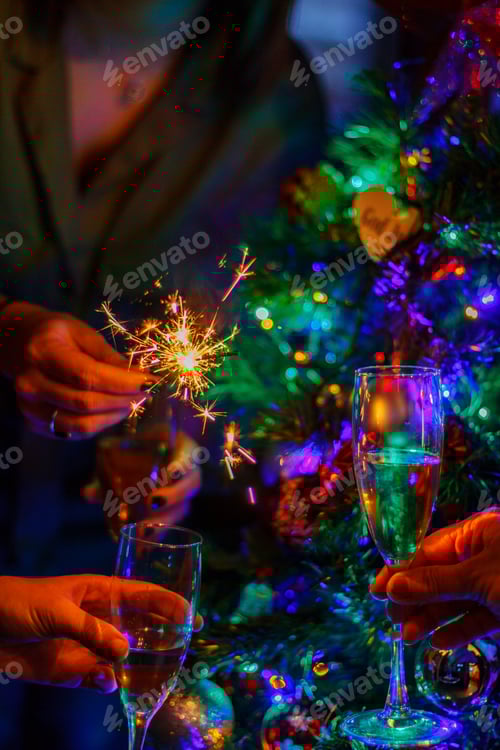 Preview: Christmas tree and hands holding glasses of champagne and a sparkler. Celebration, party