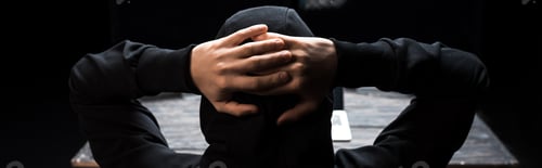 Preview: panoramic shot of hooded hacker with hands behind head isolated on black