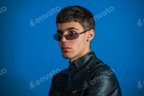 Preview: Young man wearing sunglasses and leather jacket posing on blue background