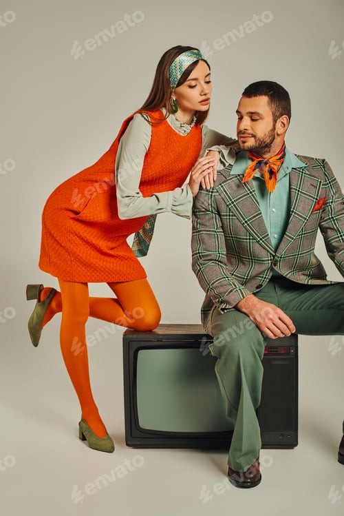Preview: charming woman leaning on shoulder of man sitting on vintage tv on grey, trendy retro couple