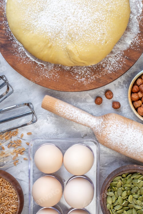 Preview: Top view of raw pastry on round wooden board grater and eggs hazel-nuts on ice background