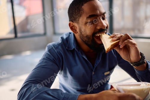 Preview: Happy black worker eating sandwich at construction site.