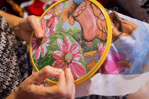 Preview: A woman embroiders with a cross. Wrinkled hands close up.