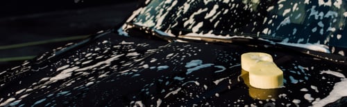 Preview: panoramic of yellow sponge on wet and luxury black automobile in car wash