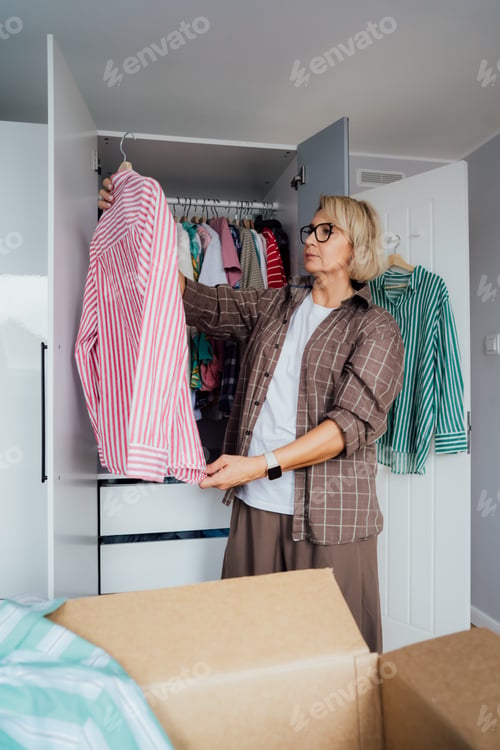Preview: Middle aged woman selecting clothes from wardrobe for donating to Charity shop. Decluttering
