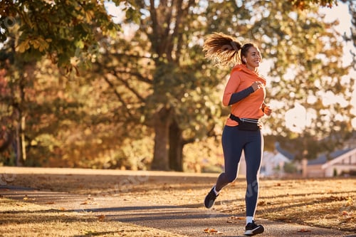 Preview: Happy athletic woman with earbuds running through the park.