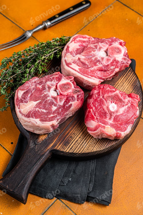 Preview: Raw lamb neck chops, fresh mutton meat on a butcher board with herbs. Orange background. Top view