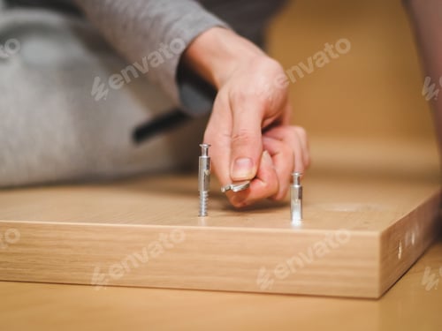 Preview: The hands of a caucasian young man with a wrench tighten a bolt on the wooden part of the bed