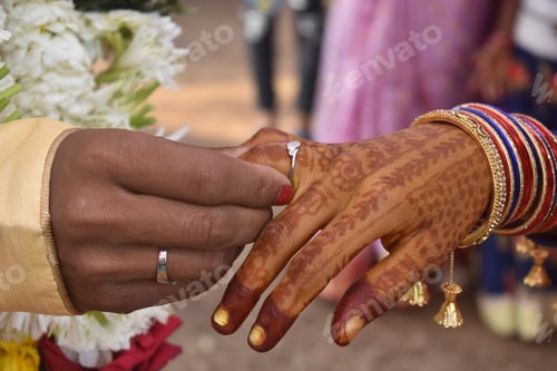 Preview: Closeup shot of an Indian couple putting on rings at their wedding