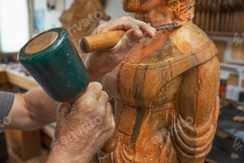 Preview: A wood carver standing in his workshop, using hand tools, mallet and chisel to shape and create