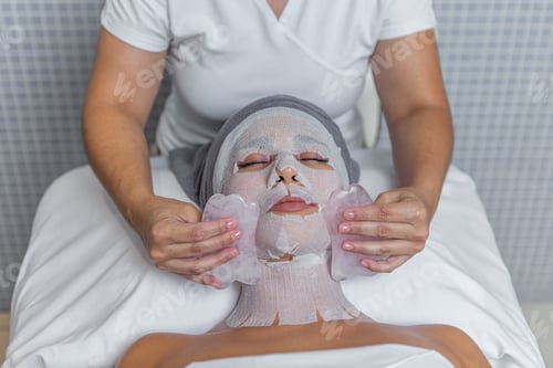 Preview: Relaxing adult woman receiving gua sha facial massage treatment by beautician in spa