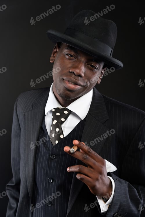 Preview: Retro African American Mafia Man Wearing Striped Suit And Tie And Black Hat. Smoking Cigar. Studio