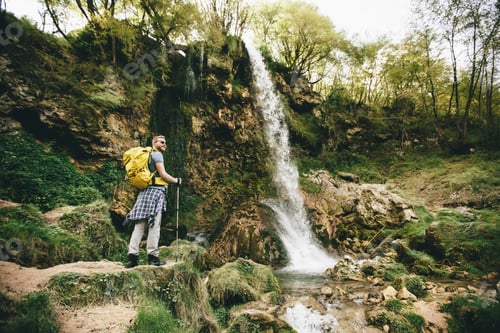 Preview: Young hiker stopped beside a mountain waterfall to rest