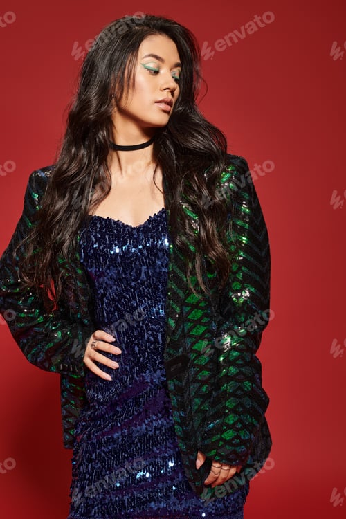 Preview: brunette asian woman in green dress and jacket with sequins posing with hand on hip on red backdrop