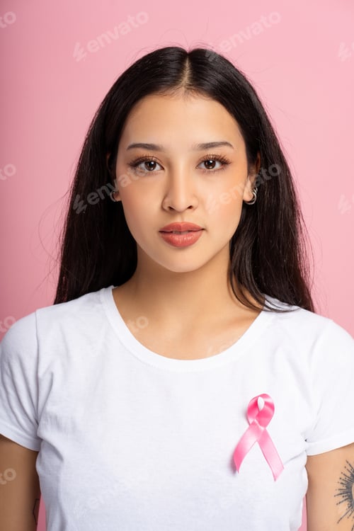 Preview: Young woman wearing pink ribbon for breast cancer awareness looking at camera