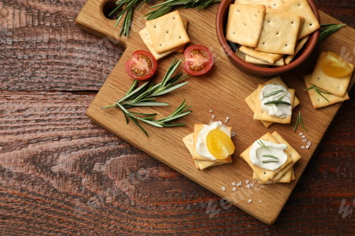 Preview: Tasty crackers with cream cheese, rosemary, salt and tomatoes on wooden table, top view