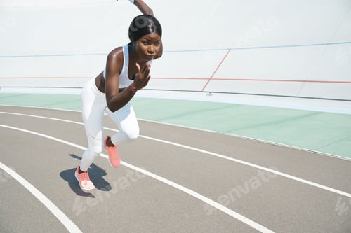 Preview: Beautiful young African woman in sports clothing running on track outdoors