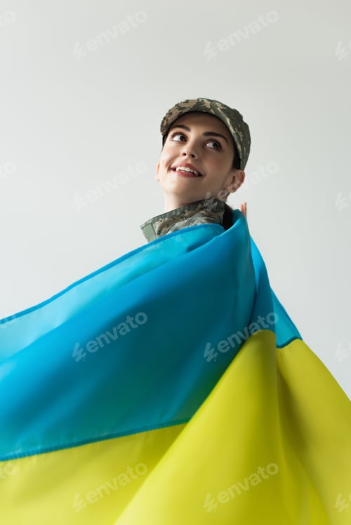 Preview: Smiling soldier in uniform and ukrainian flag looking away isolated on grey